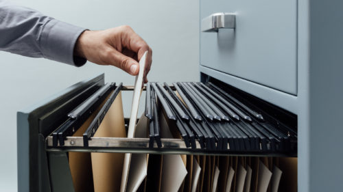 Office clerk searching for files into a filing cabinet drawer close up business administration and data storage concept