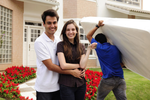 Real estate and moving home: Couple showing keys and relocator carrying mattress into their new home