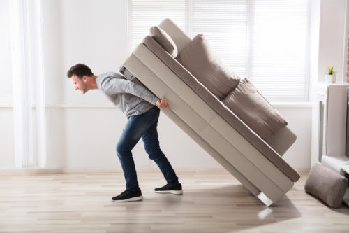 Young Man Trying To Move Sofa At Home