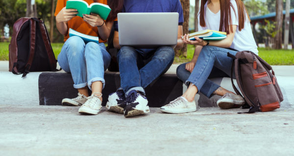 College kids sitting on a curb with textbooks and laptops